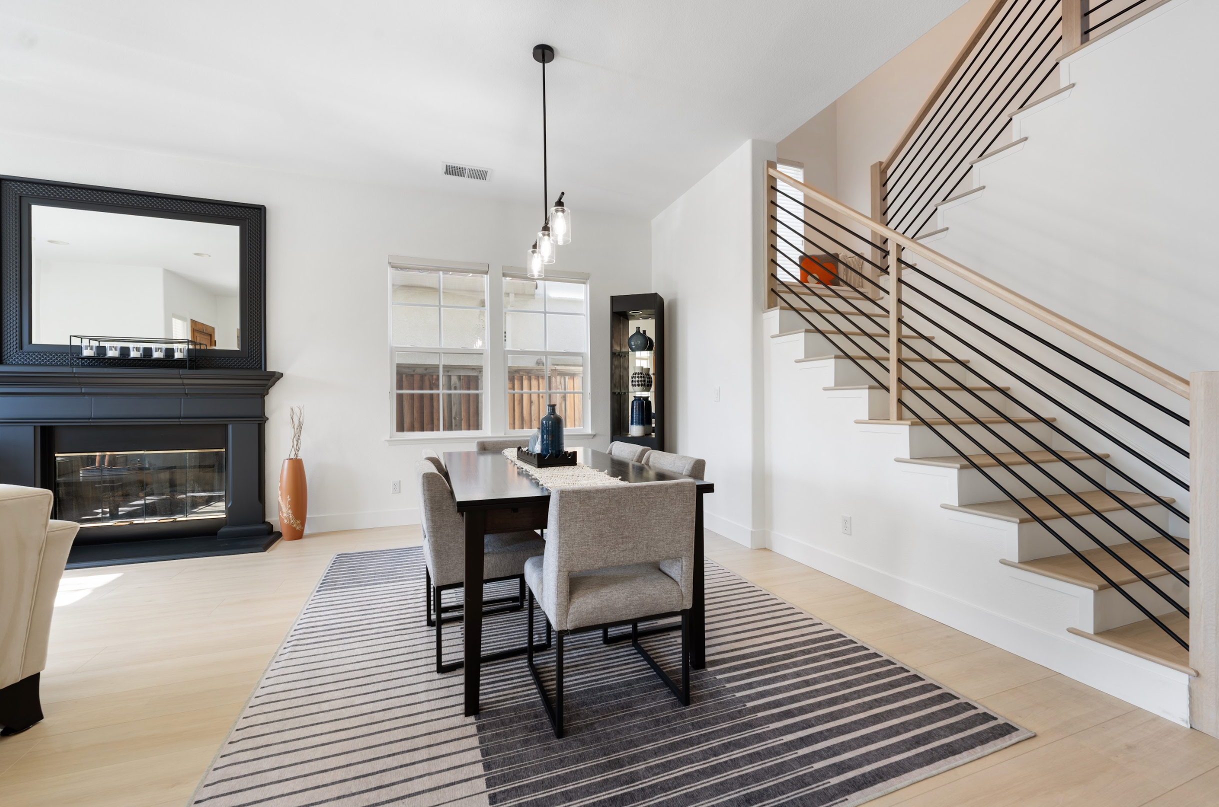 Modern living room with a dining area, fireplace, and staircase.